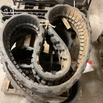 Stack of large, rugged tires with deep treads stacked on a wooden pallet in a workshop, dusty and used.